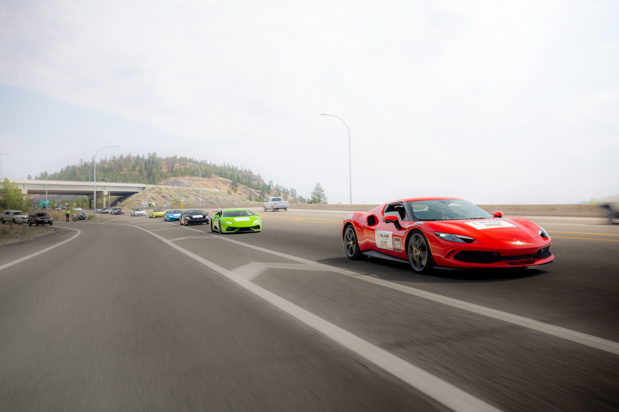 Red Ferrari leading a line of exotic cars onto Highway 97