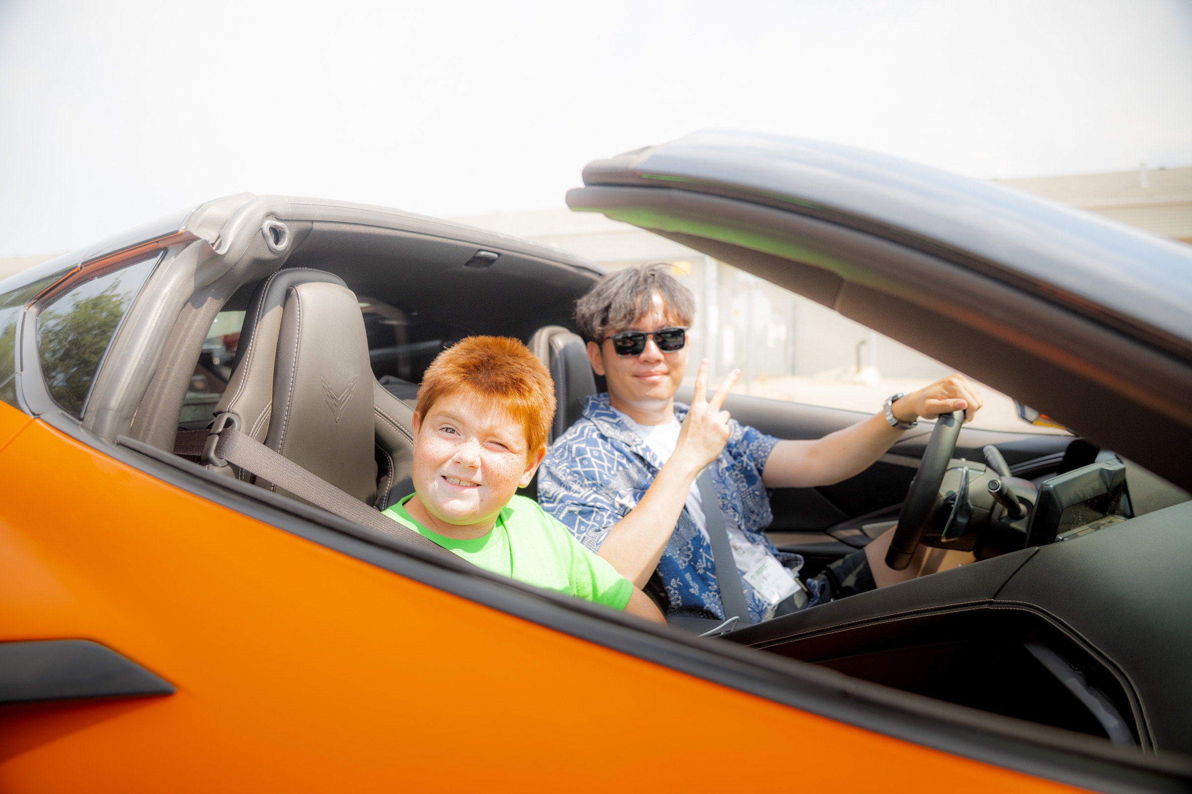 Young Dream Rally co-pilot and driver smiling from an orange Corvette