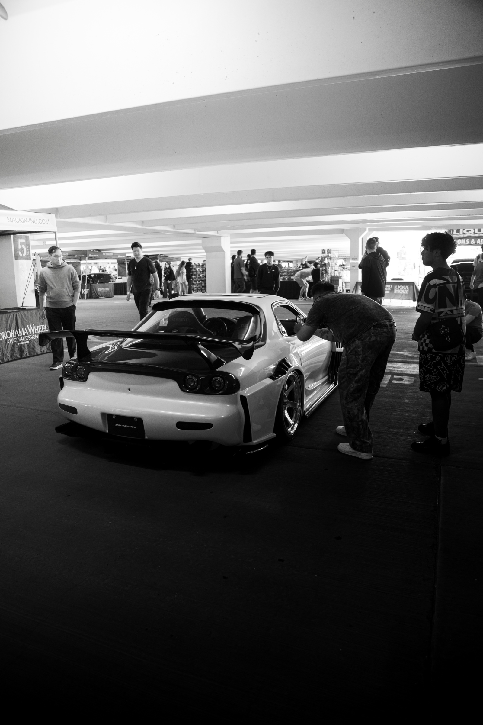 Black-and-white view of a modified Mazda RX-7 and attendees