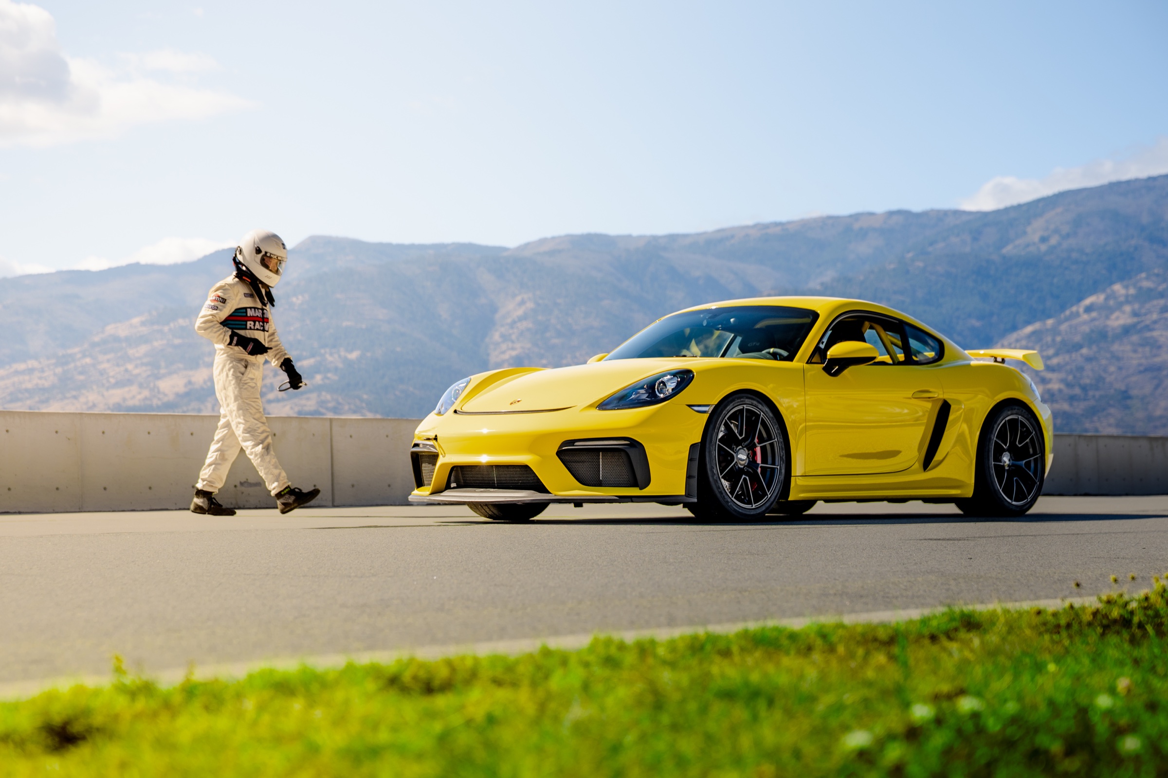Driver walking toward a yellow Porsche 718 Cayman GT4 at Area 27