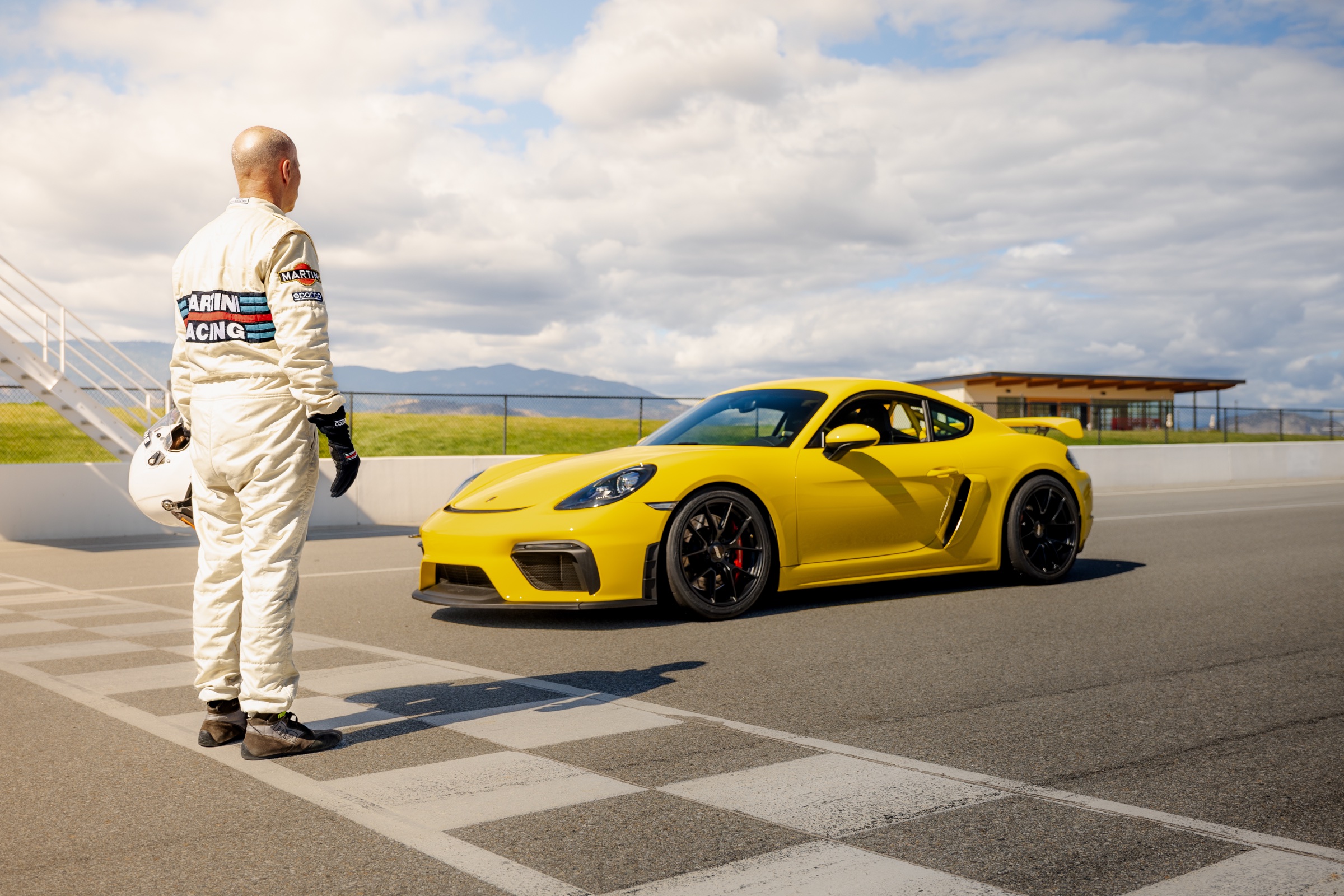 Driver facing a yellow Porsche 718 Cayman GT4 on the starting grid