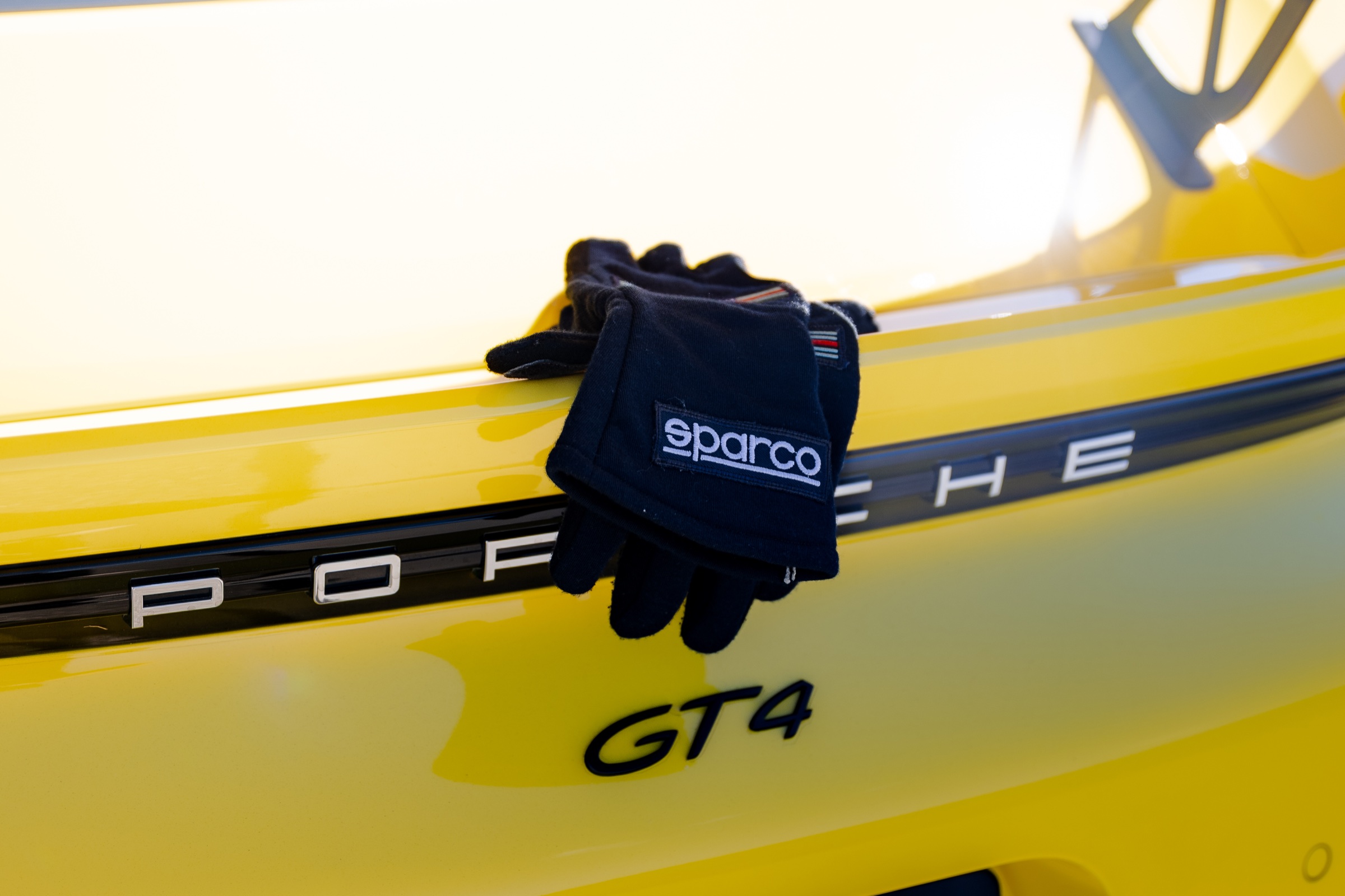 Sparco racing gloves resting on the rear of the yellow Porsche GT4