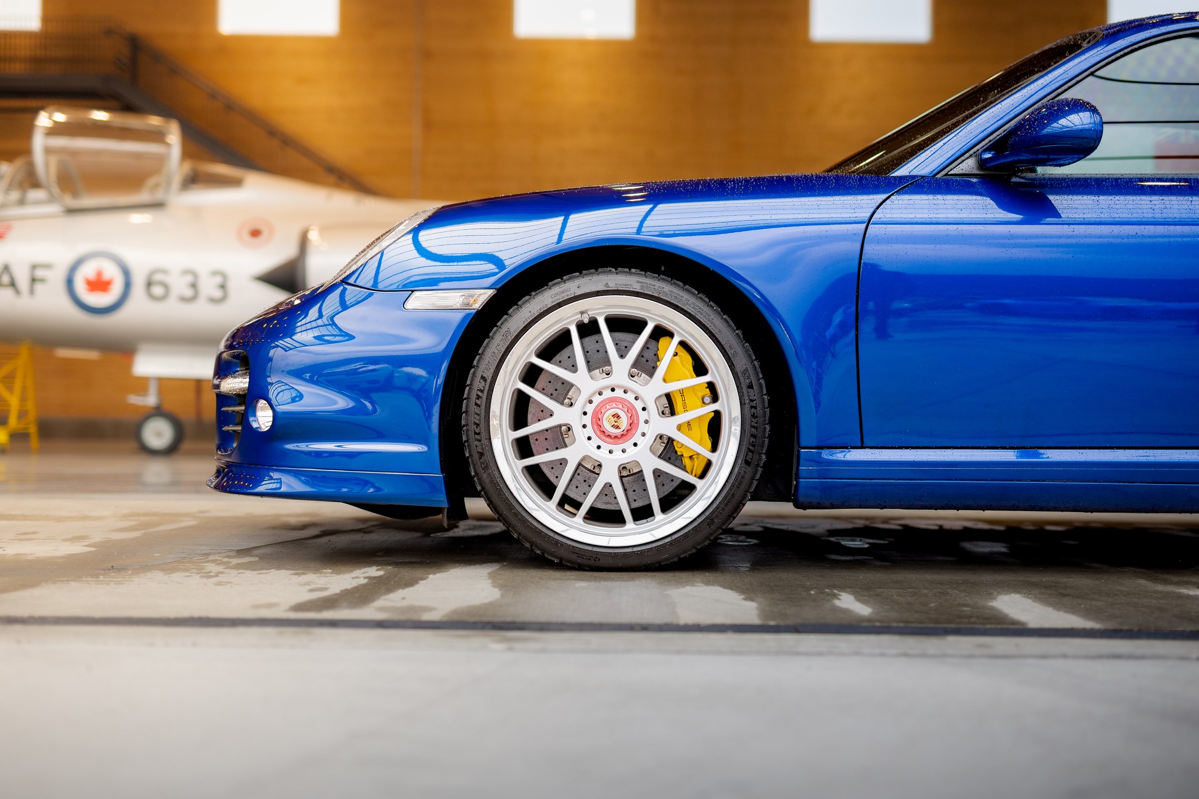 Blue Porsche front wheel framed against an RCAF aircraft