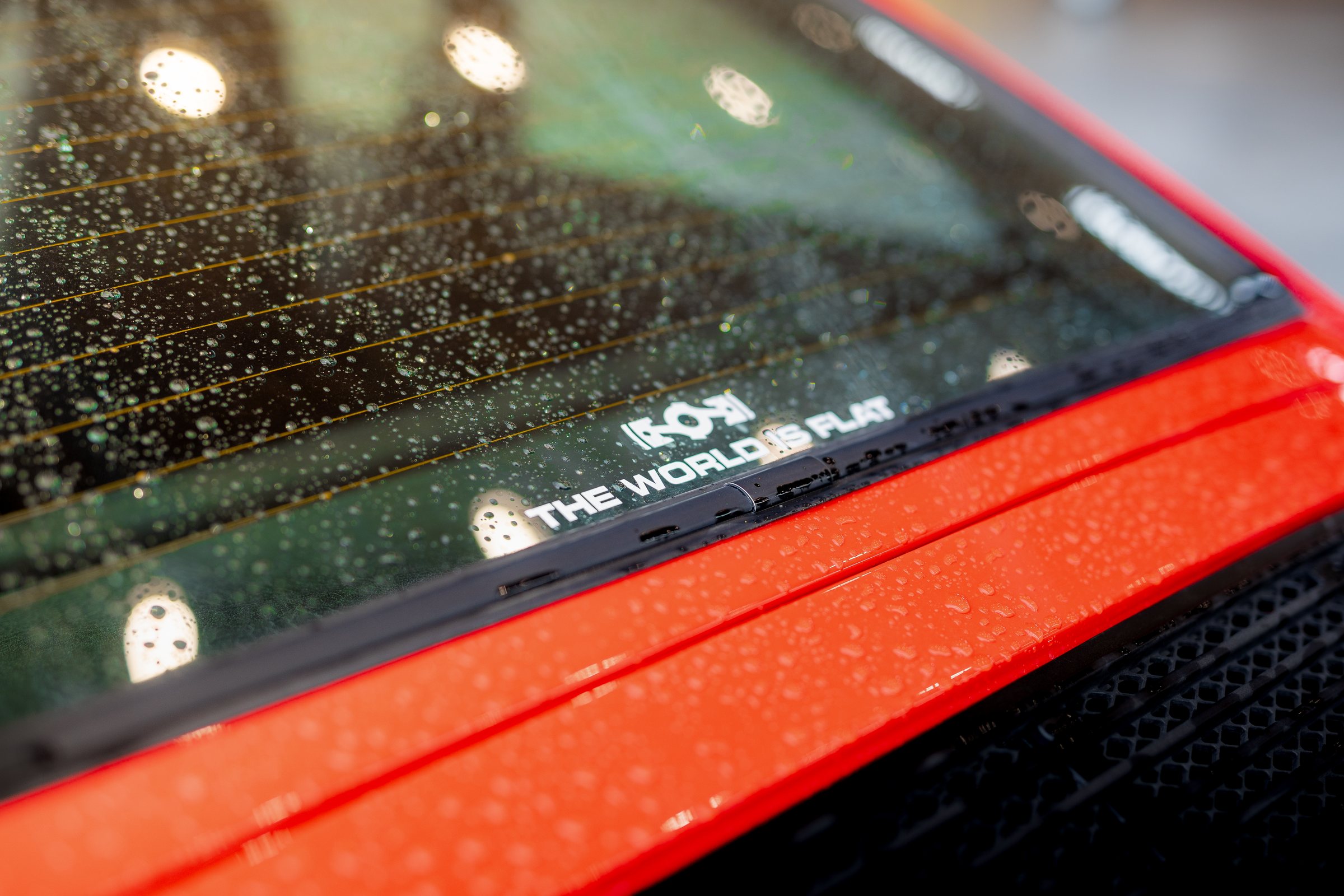 RWB decal on the rain-covered rear glass of a red Porsche