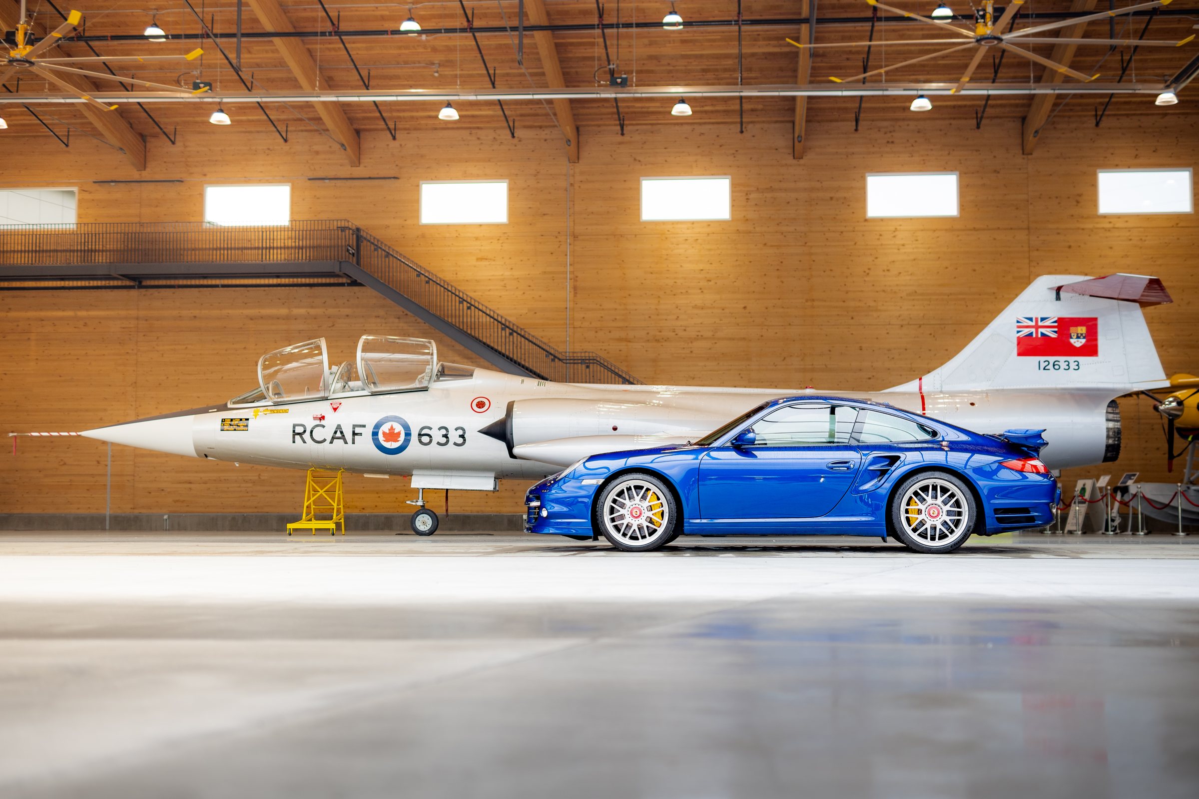 Blue Porsche 911 Turbo profiled beside an RCAF aircraft