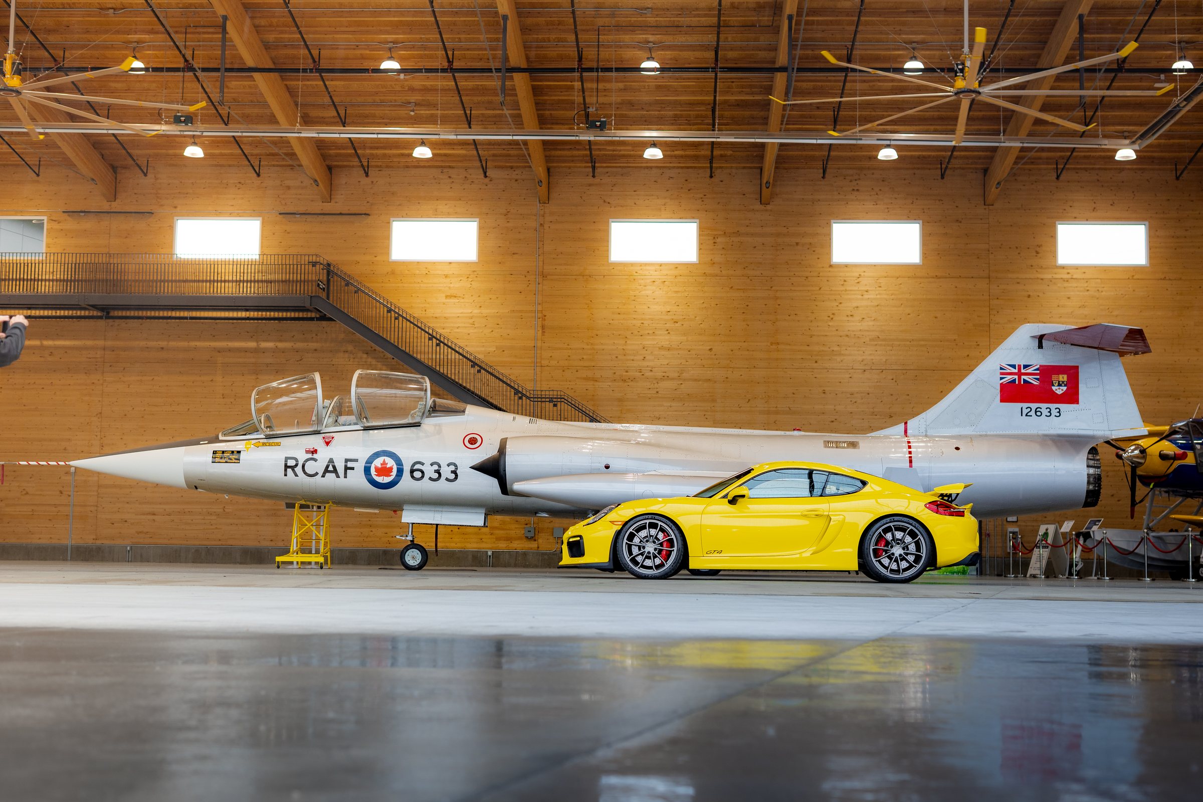 Yellow Porsche Cayman GT4 profiled beside an RCAF aircraft