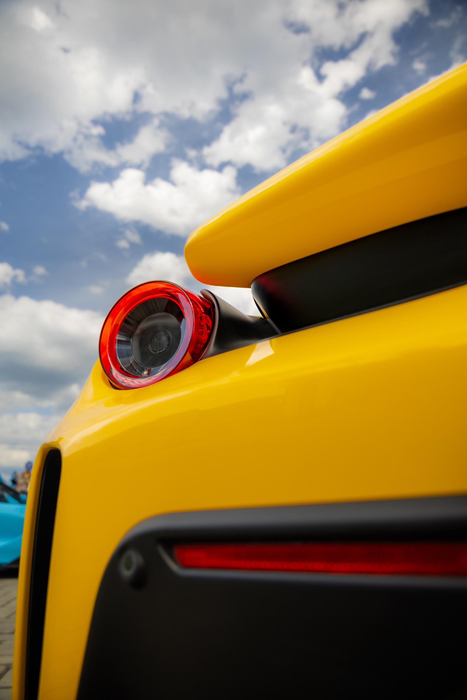 Low-angle rear detail of a yellow Ferrari against a summer sky